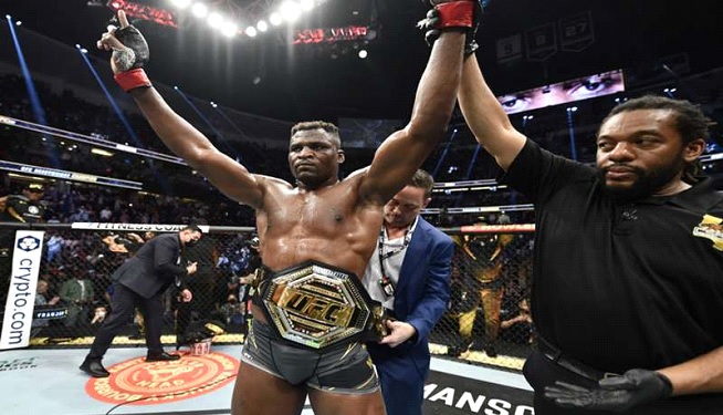 Francis Ngannou raising his hand in victory in a UFC match after displaying professional fighting technique.