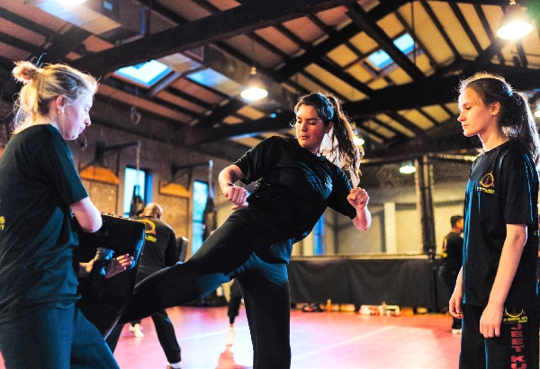 Two kickboxers train with the striker sending a low kick into the training pad at shin level.