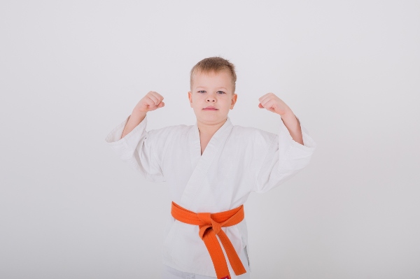 When you choose martial arts for your child, they will gain physical and emotional strength like the child flexing in his gi in this picture.