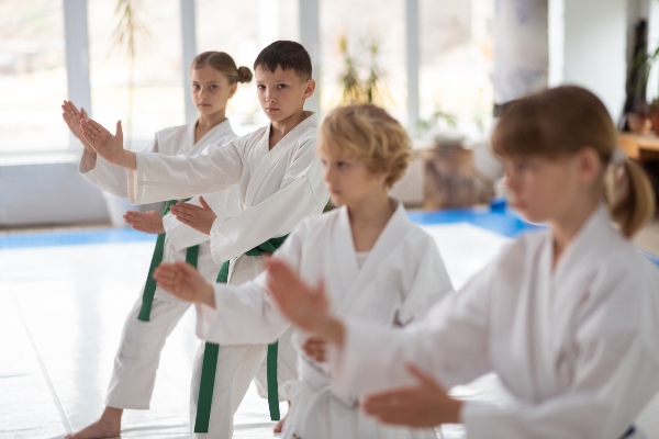 Children stand ready in a martial arts class while one boy looks directly at the camera.