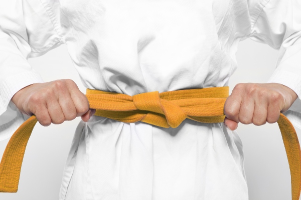 A karate student tightens their orange belt.