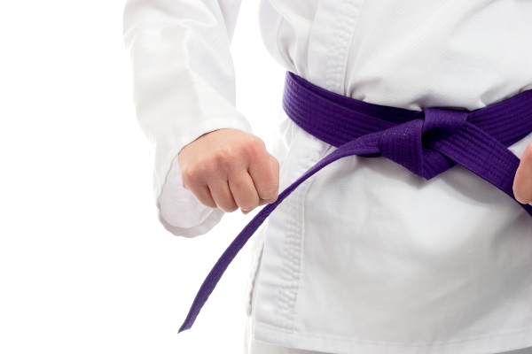A karate student tightens their purple belt.
