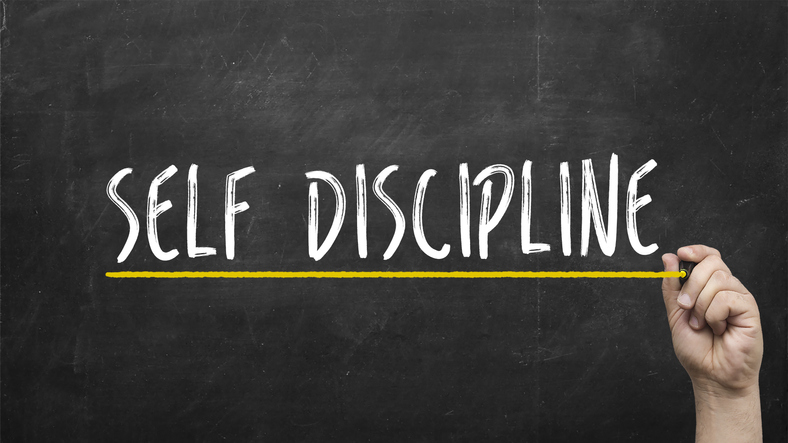 A hand has written the words self discipline on a chalkboard.
